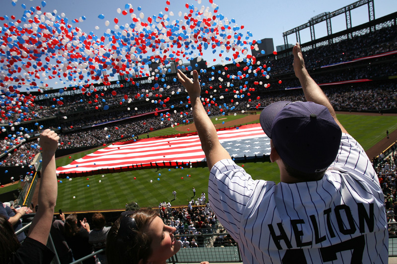 Alyssa Alcorta, 19, center bottom, looks up to friend, Andrew Baker, 21, as he stretches his arms out to balloons being released during the opening ceremonies before the Colorado Rockies first home game of the season with the Arizona Diamondbacks at Coors Field in downtown Denver. Photo by Matt McClain