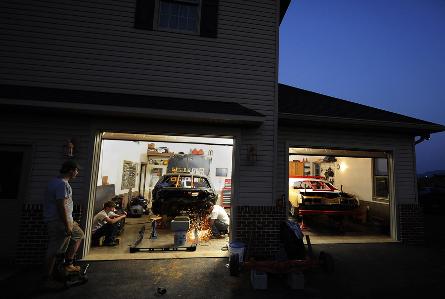 Zach Orndorff, left, and his brother, Josh Orndorff, left center, watch their father Bill Orndorff, center, work on Zach's demolition derby car at the family's Woodstock, VA home on Tuesday August 21, 2012 in Woodstock, VA.  